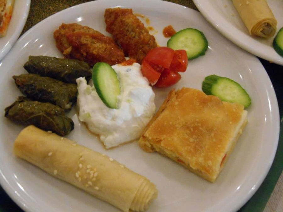 plate from above with fried rolls meet and pie and yogurt and slices of cucumber and cutting tomato cherry